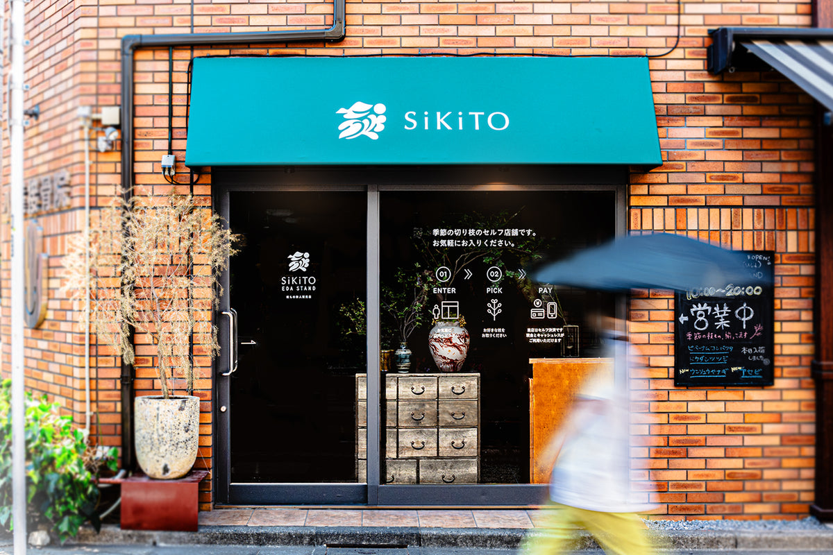 SiKiTO EDA STANDの店舗のまえを女性が通過しているところ